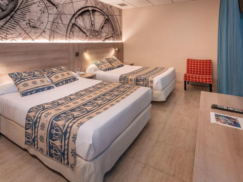 Chambre d'hôtel avec deux lits, feuilles décoratives sur le mur et une chaise rouge dans la pièce.