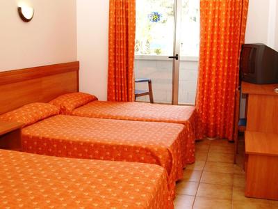 Habitación de hotel con tres camas individuales, cortinas naranjas y TV en muebles de madera.