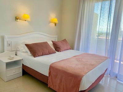 Brightly furnished bedroom with double bed, pink bedspread, and large window with curtains.