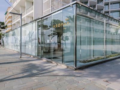 Edificio moderno di un hotel con facciata in vetro e pavimentazione in pietra all'aperto sotto un cielo sereno.