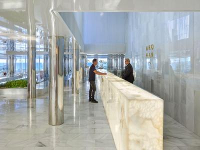 Reception di un hotel moderno con un lungo bancone in marmo e due persone al banco.