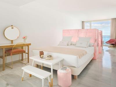 Camera moderna con letto bianco, pannelli rosa e vista sul mare.