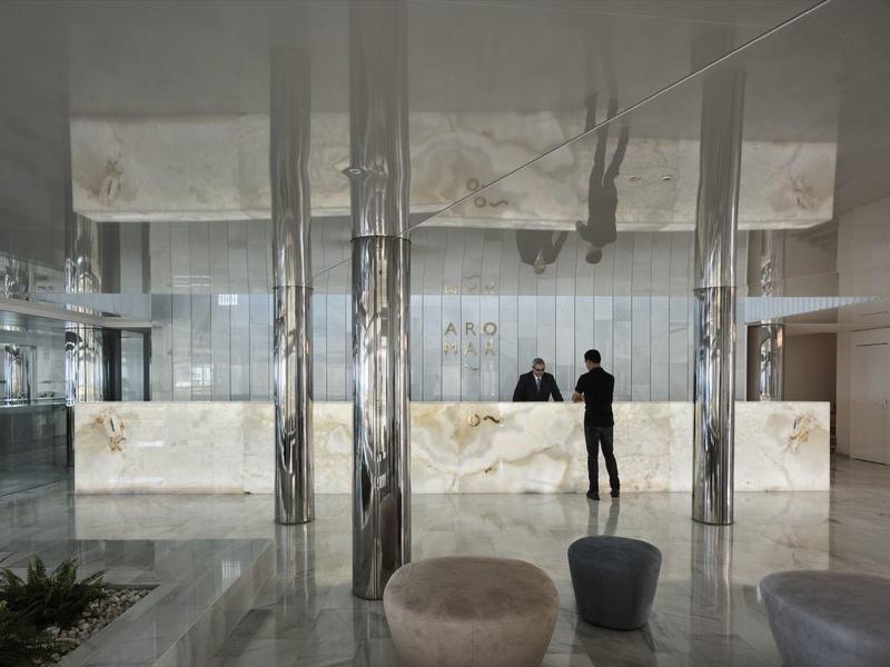 Modern hotel lobby with two marble reception desks and two people in the background.