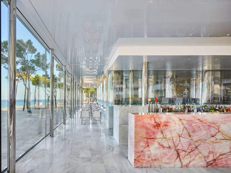Modern bar area with glass front, view of palm trees and the sea.