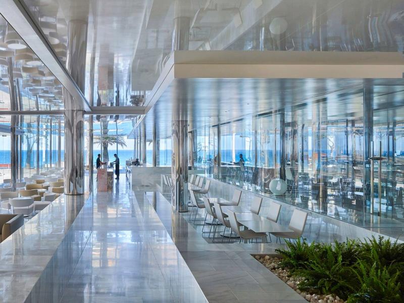 Modern waiting area with white benches and large glass windows overlooking the sea.