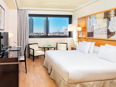 Chambre d'hôtel lumineuse avec lit double, coin salon, grande fenêtre et vue sur la ville.