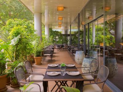 Une terrasse d'hôtel avec des tables dressées et des chaises à côté de grandes plantes.