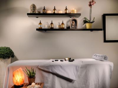 Salle de bien-être confortable avec table de massage, lampe de sel et étagères décoratives au mur.