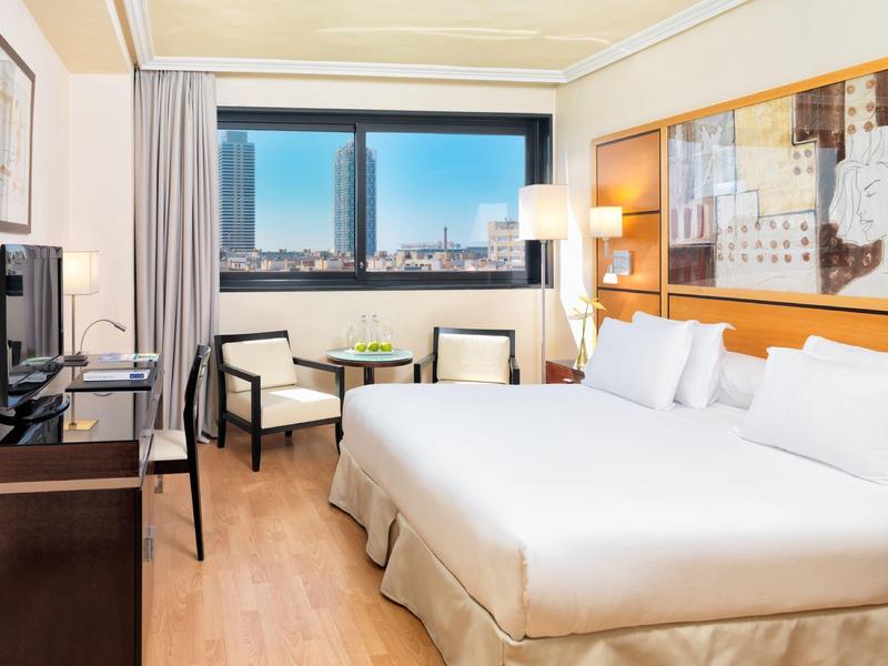 Lichte hotelkamer met tweepersoonsbed, twee stoelen en uitzicht op de stad door groot raam.