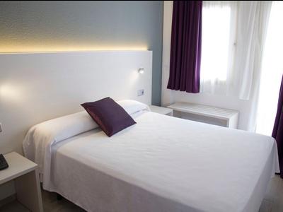 Moderne slaapkamer met wit bed, paarse kussen en gordijnen, en een raam.