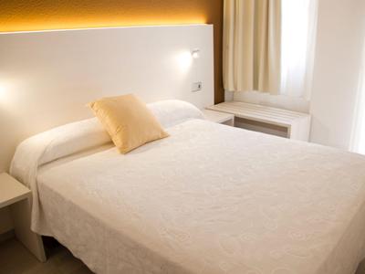 Lichte, moderne slaapkamer met een groot bed, twee nachtkastjes en zacht licht.