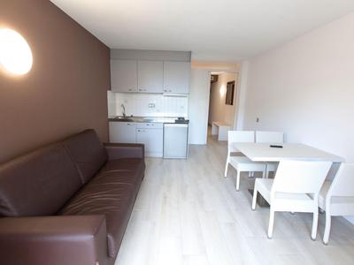 Modern appartement met bruine bank, witte eettafel en kitchenette in lichte kamer.