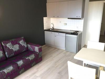 Kleine kitchenette met gootsteen, koelkast en fornuis naast een tafel en een paarse bank.