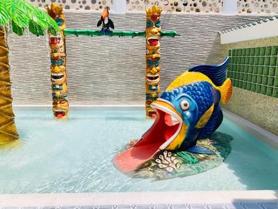 Bunter Fischrutsche im Wasserbecken mit Palmen und Felsenmauer im Hintergrund.