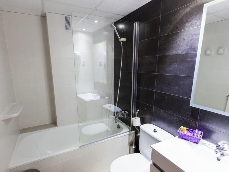 Nowoczesna łazienka z białą wanną, ciemną ścianą z płytek i białą toaletą obok.