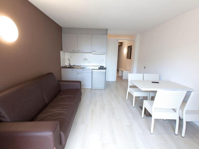 Nowoczesny salon z brązową kanapą, białym stołem jadalnym i niewielką kuchnią.