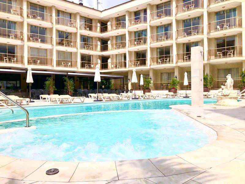 Zewnętrzny basen hotelowy otoczony leżakami i balkonami w słoneczny dzień.