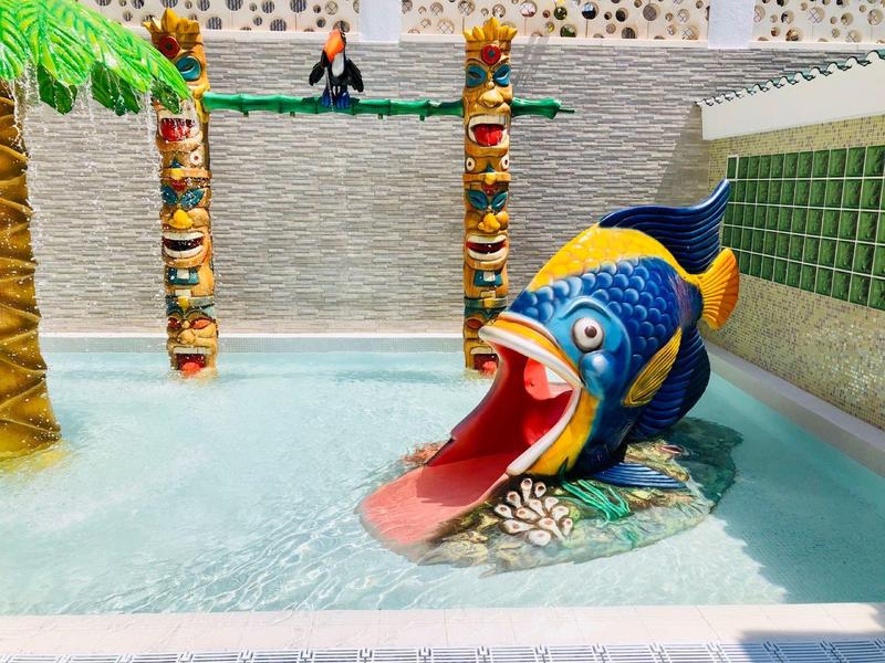 Plac zabaw wodny dla dzieci z kolorową zjeżdżalnią w kształcie ryby i dekoracyjnymi słupami tiki