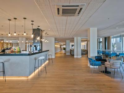 Nowoczesny bar hotelowy z drewnianą podłogą, wiszącymi lampami, miejscami do siedzenia i dużymi oknami.