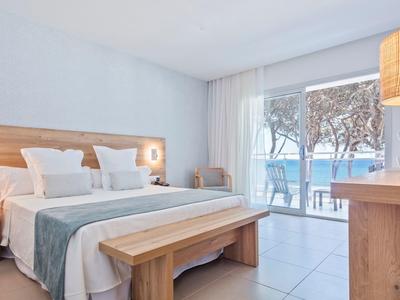 Habitación de hotel luminosa con cama doble, muebles de madera y vista a la terraza y el mar.