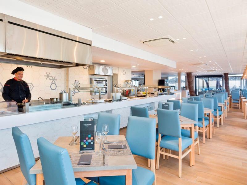 Comedor moderno con sillas azules y barra larga, ambiente luminoso y espacioso.