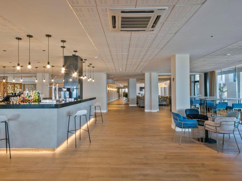 Amplio lobby de hotel moderno con bar, sillas altas y zona de descanso luminosa y espaciosa