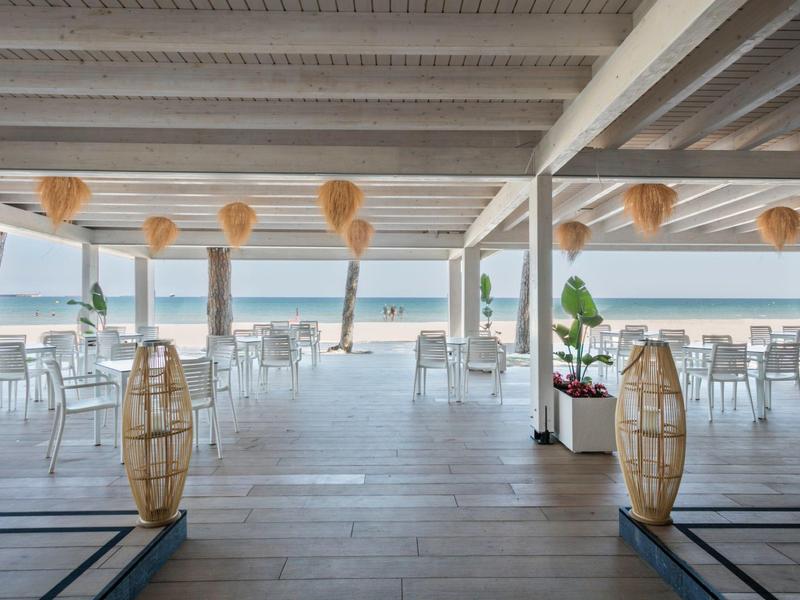 Restaurante abierto y luminoso con mesas y sillas blancas con vistas al mar bajo un techo de madera.
