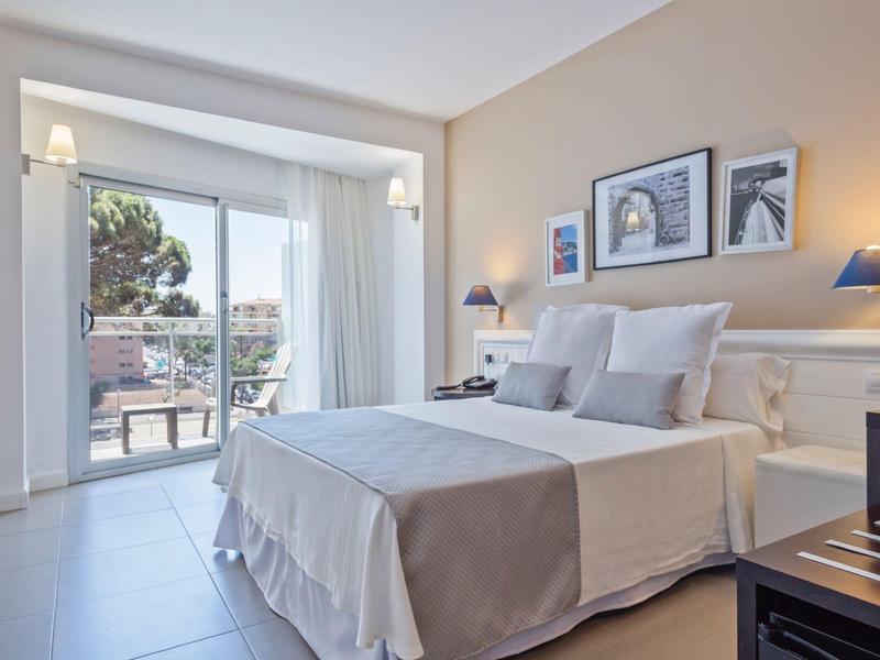 Habitación de hotel luminosa con cama doble, iluminación moderna y balcón con vista a árboles.