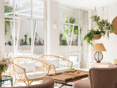 Helles Wohnzimmer mit großen Fenstern, Korbmöbeln und vielen grünen Pflanzen.