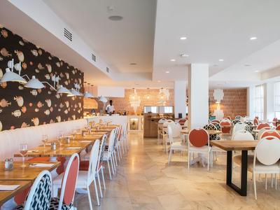 Helles modernes Restaurant mit Holzfußboden, weißen Wänden und bunten Stühlen.