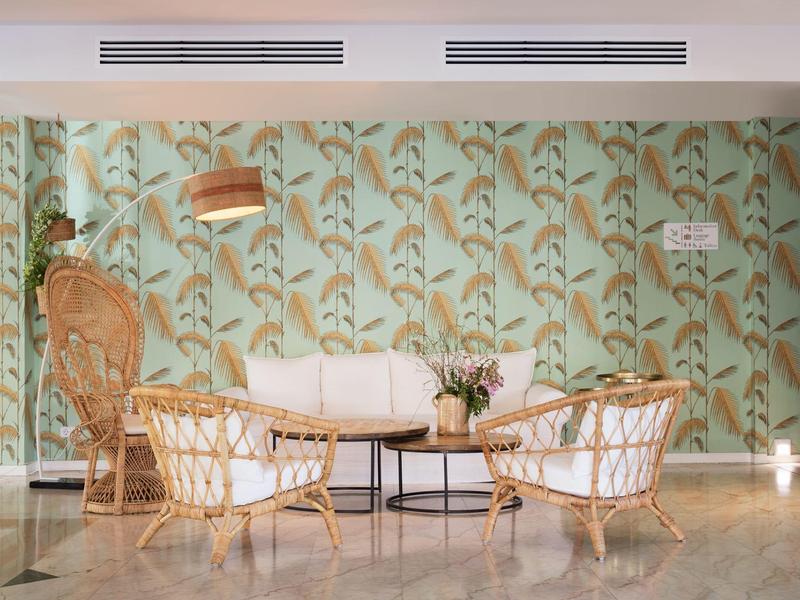 Salon confortable avec mobilier en bambou et motif de feuilles vertes sur le mur dans un hôtel.