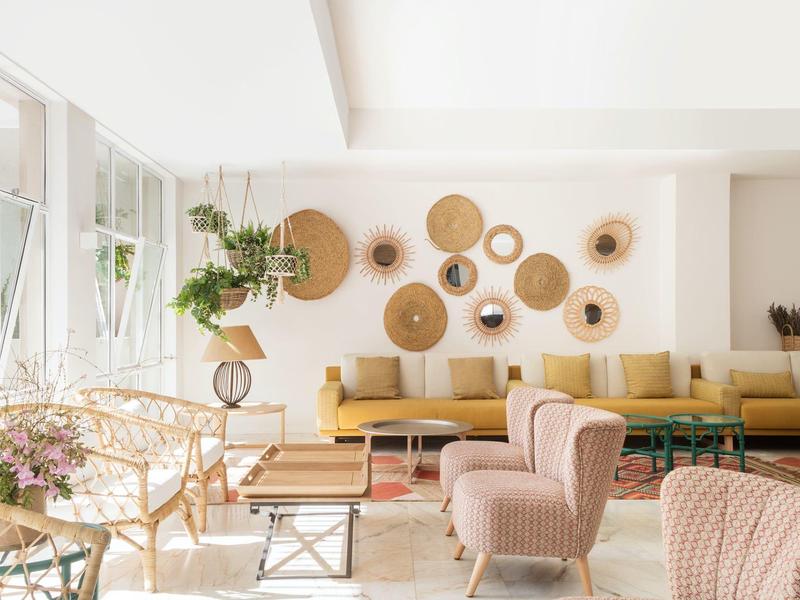 Chambre d'hôtel lumineuse avec canapé jaune, fauteuils roses et paniers muraux décoratifs.