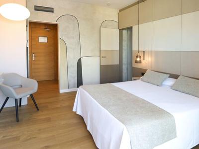 Helles Hotelzimmer mit Doppelbett, grauer Akzentwand und modernem Stuhl.