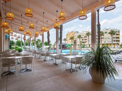 Offener Hotelrestaurantbereich mit Tischen, Stühlen und Blick auf einen Pool und angrenzende Gebäude.