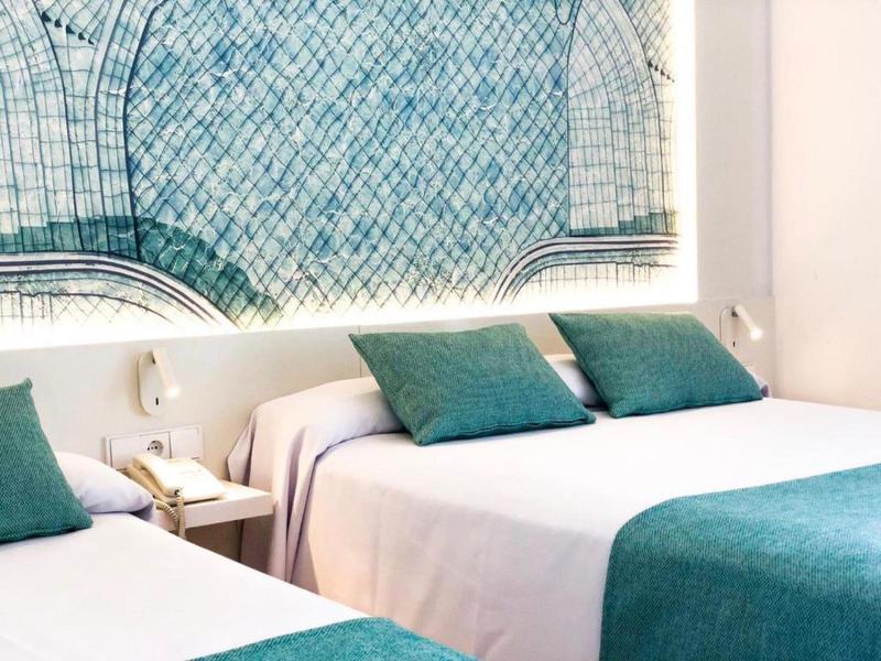 Modern eingerichtetes Hotelzimmer mit Doppelbett, grünen Kissen und abstrakter Wandkunst.