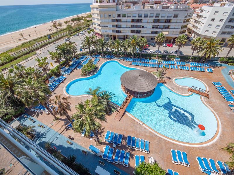 Großer Außenpool in Hotelanlage mit Liegestühlen, Sonnenschirmen und Blick aufs Meer.
