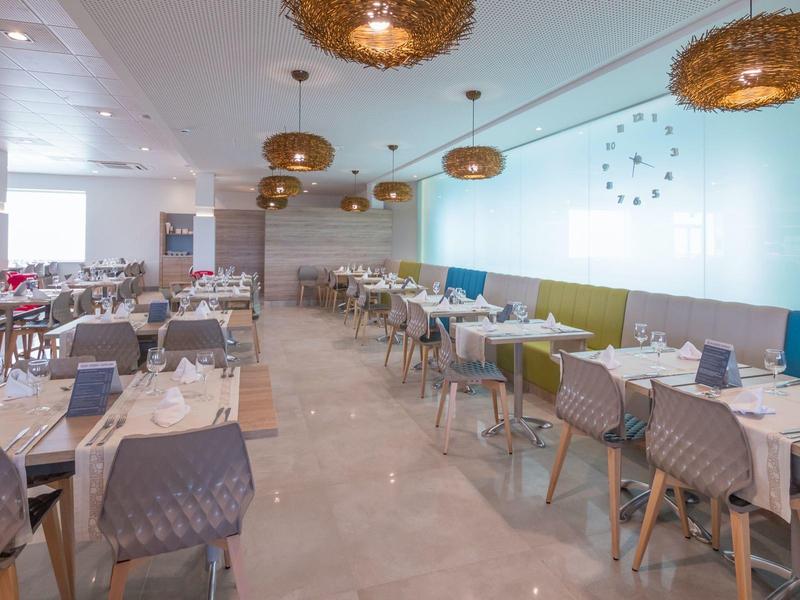 Modernes Restaurant mit eleganten Tischen, Stühlen und Korbhängelampen in hellem Ambiente.
