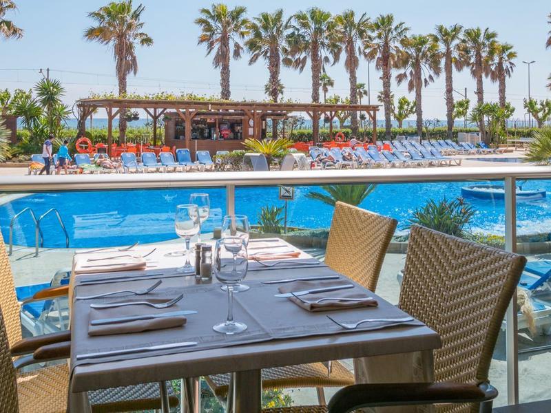 Terrasse mit gedeckten Tischen und Blick auf einen Pool und Palmen bei klarem Himmel.