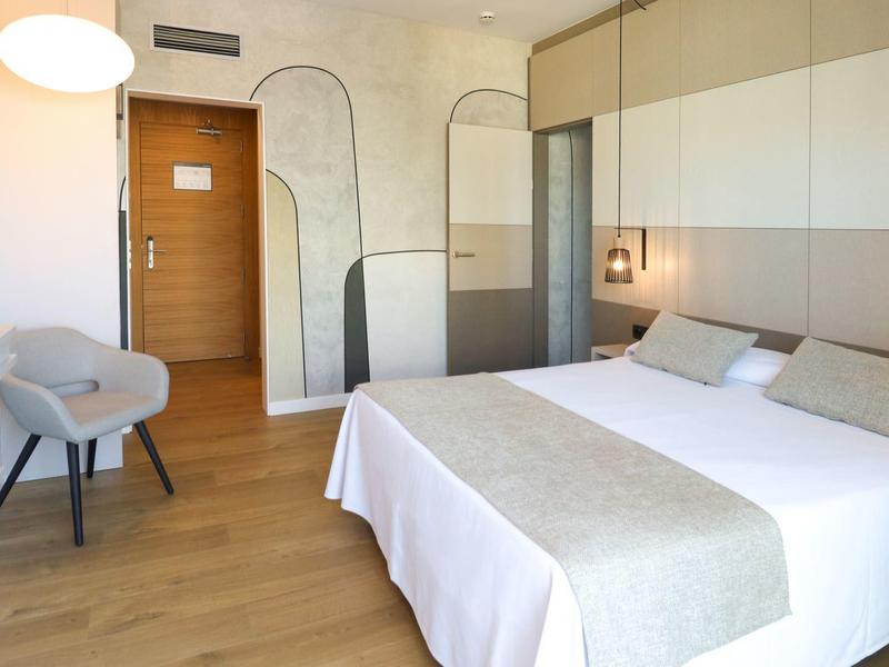 Helles Hotelzimmer mit Doppelbett, grauer Akzentwand und modernem Stuhl.