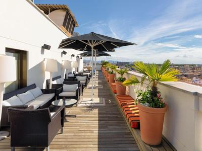 Terrazza sul tetto con posti a sedere, ombrelloni, piante e vista sulla città.