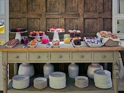 Buffet con vari frutti, pasticcini e bevande su un tavolo di legno con piatti sotto.