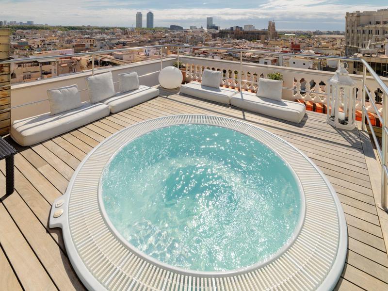 Střešní jacuzzi obklopené posezením s výhledem na město pod zataženou oblohou.