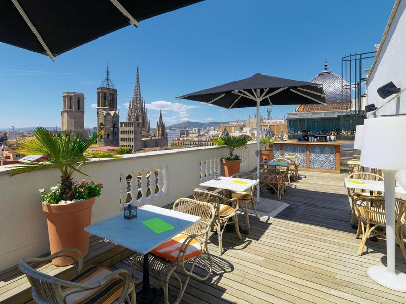 Slunečná střešní terasa s stoly, židlemi, slunečníky a výhledem na město.