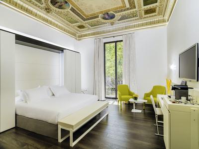 Helles Hotelzimmer mit weißen Möbeln, dekorativer goldener Decke und großen Fenstern.