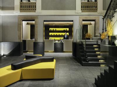 Moderne Lobby mit schwarzen und gelben Sitzmöbeln, grauem Boden und dezenter Beleuchtung.