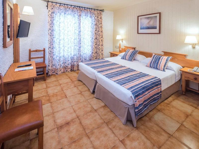 Licht ingericht hotelkamer met twee eenpersoonsbedden, bureau en flatscreen-tv.