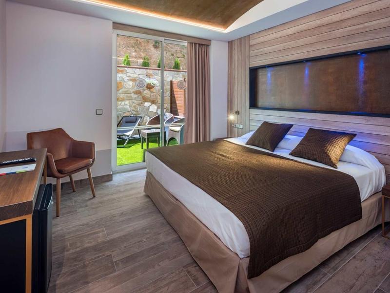 Moderne hotelkamer met tweepersoonsbed, stoel, tv en uitzicht op tuin en terras.