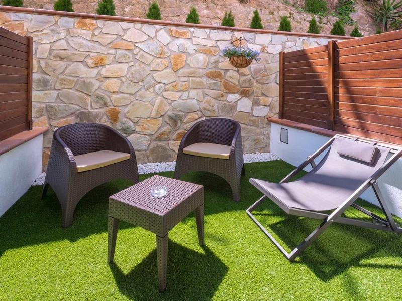 Gezellig zitgedeelte met stoelen en ligstoelen op kunstgras naast houten wanden.