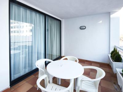 Balkon s bílým kulatým stolem a čtyřmi bílými plastovými židlemi u hotelového pokoje.