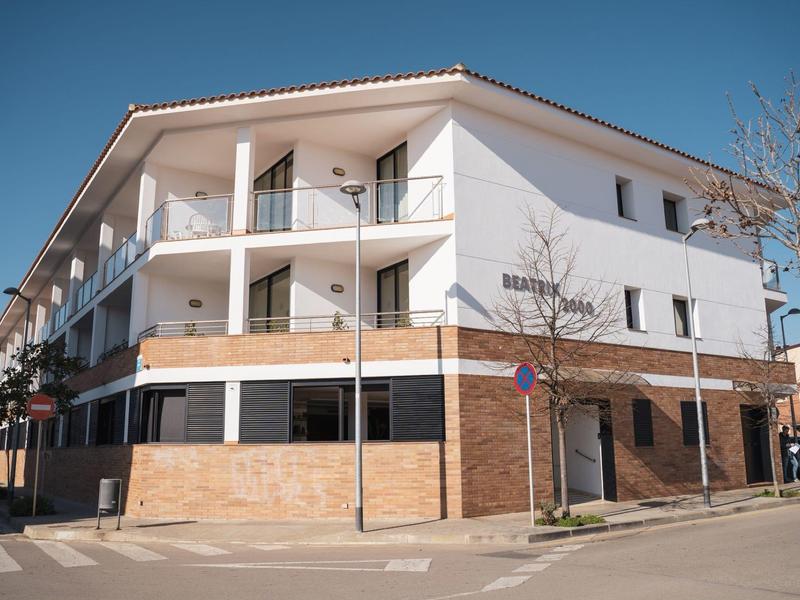 Moderní třípodlažní budova s bílými zdmi a dřevěnými doplňky na rohu ulice.